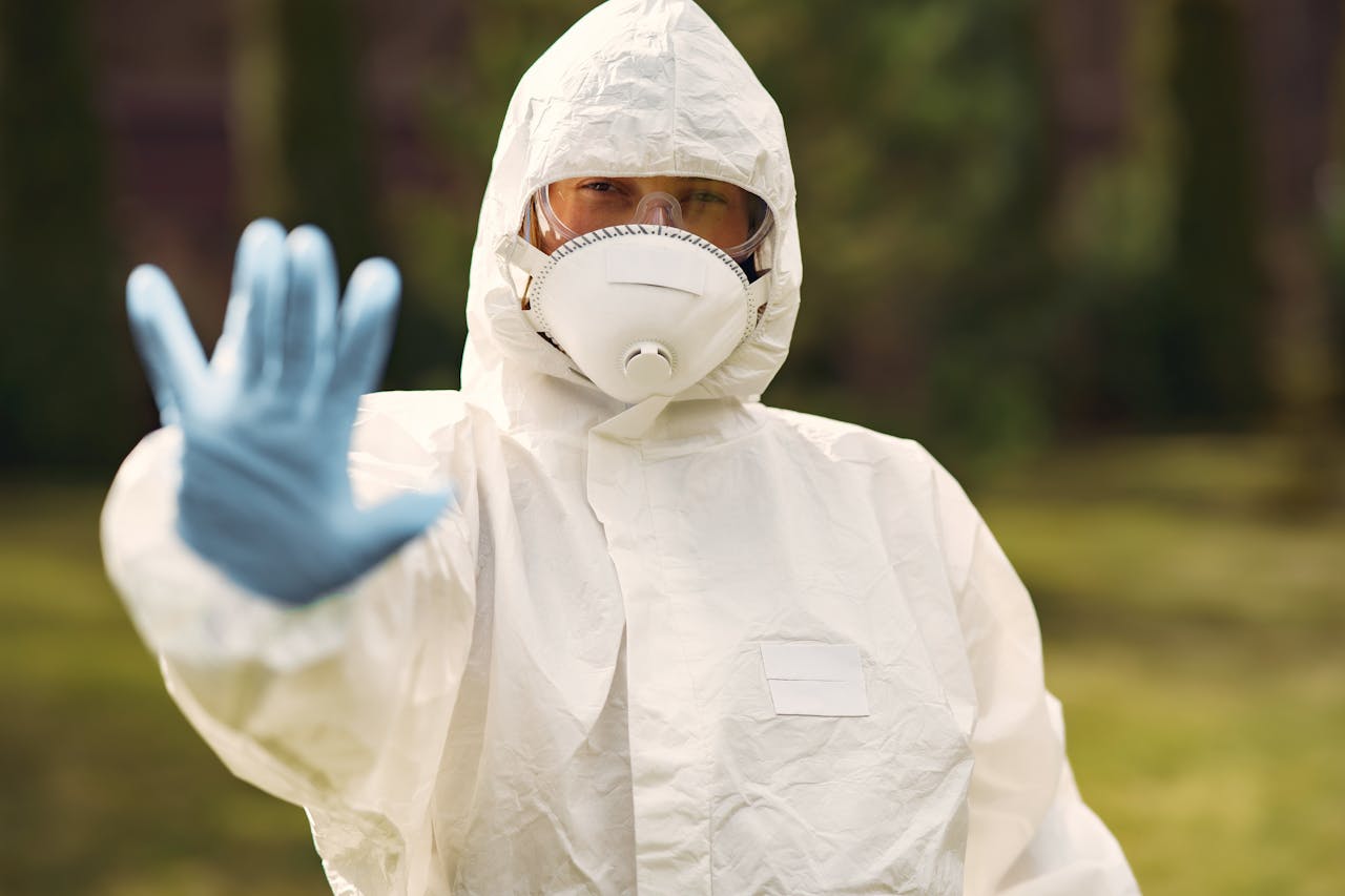 Person in protective equipment outdoors with hand raised, symbolizing caution and safety.